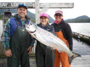 Three fisherman standing on a dock holding up a Salmon.