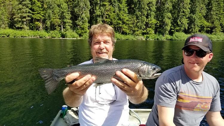 Two Fisherman sitting in a boat while one holds up a Rainbow Trout.